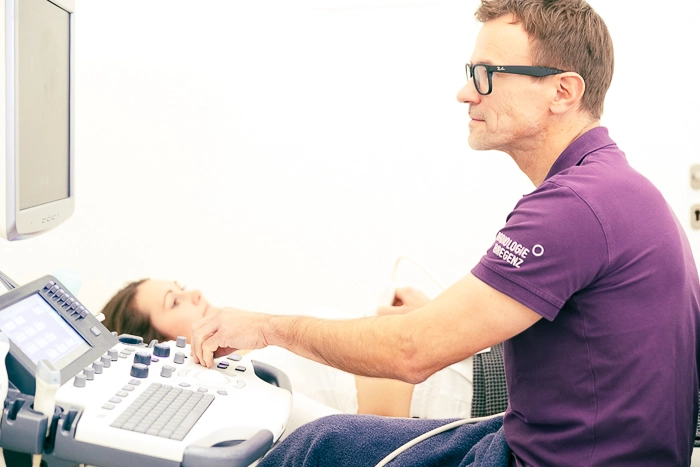 Ein Arzt in einem magentafarbenen Poloshirt führt eine Untersuchung im Ultraschall durch.